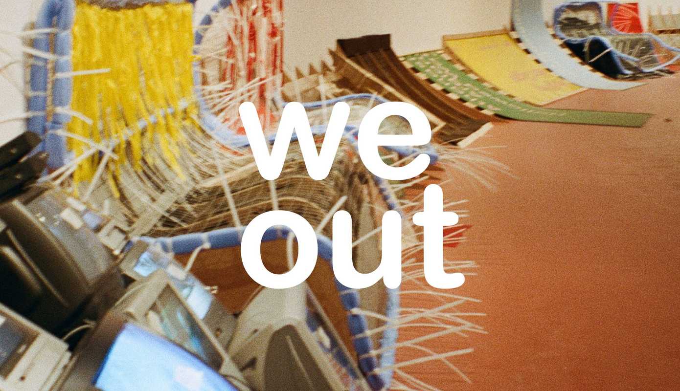 The text 'we out' sits on top of a film image taken of RESOLVE's exhibition 'them's the breaks'. There is a series of makeshift chairs and installation furniture lined up against a curved wall.